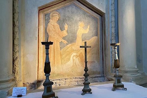 Affresco religioso in una chiesa, raffigurante un santo in preghiera, con tre candelabri e una croce in primo piano