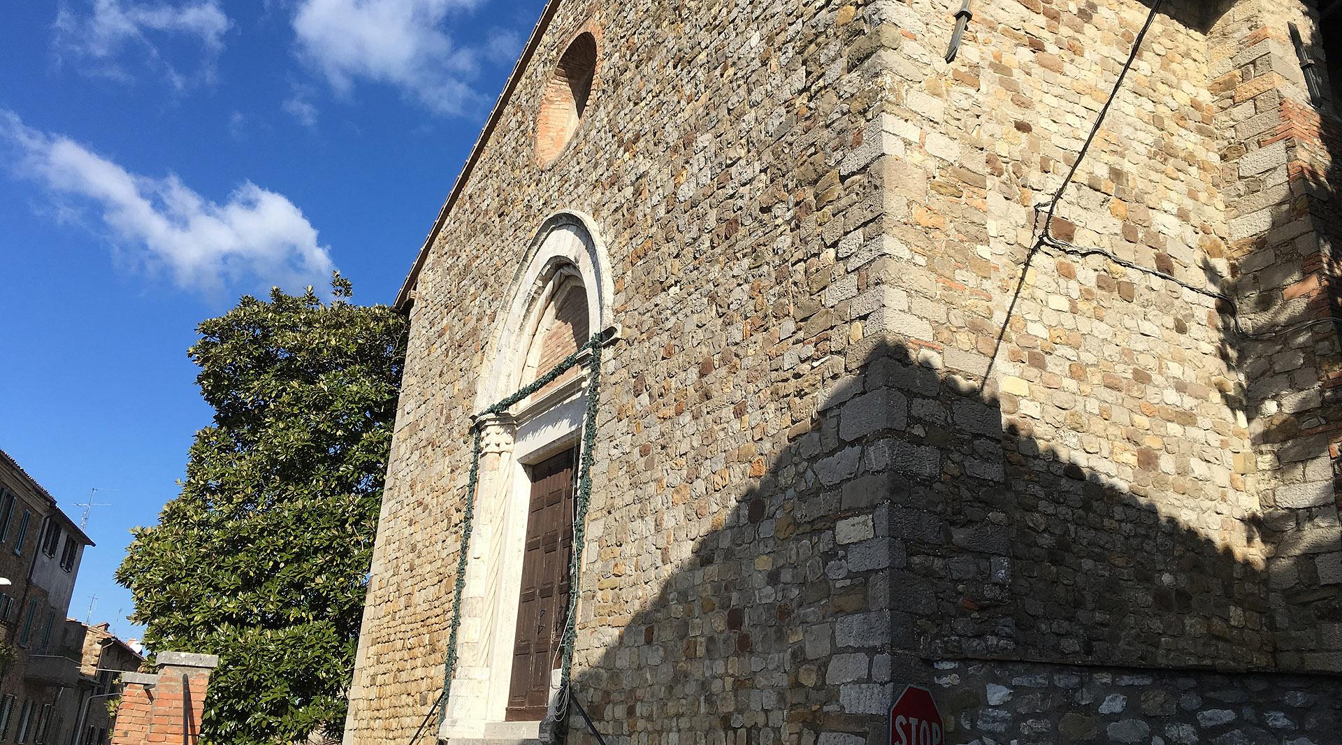 Stone façade of the Church of Santa Maria Vecchia in Ficulle, sunlit against a bright blue sky.