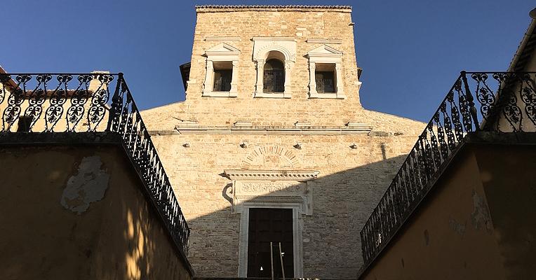 Steinfassade der Basilika San Salvatore mit Treppe und Eisenbalustraden, beleuchtet vom Licht des Sonnenuntergangs.