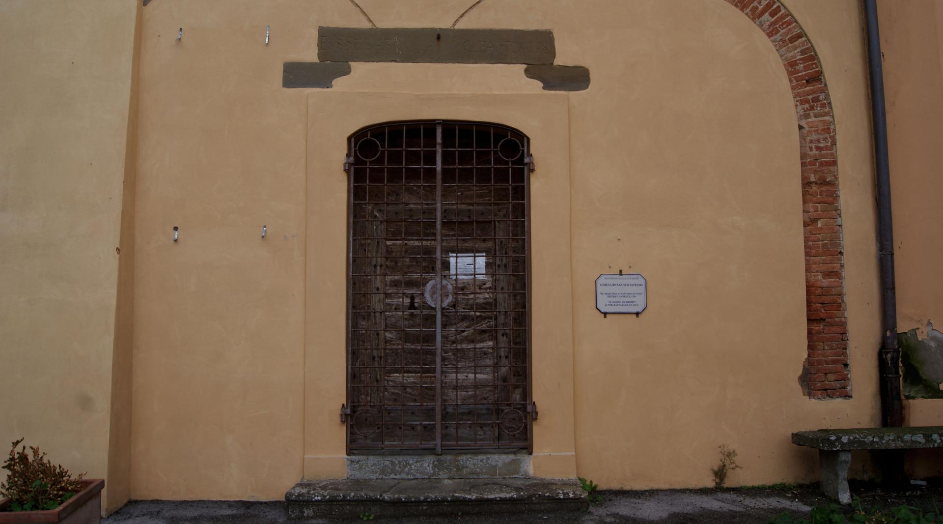 Detail of the front façade of the Church of San Sebastiano, covered in plaster. In the center, a brick arch sits above the main entrance door.