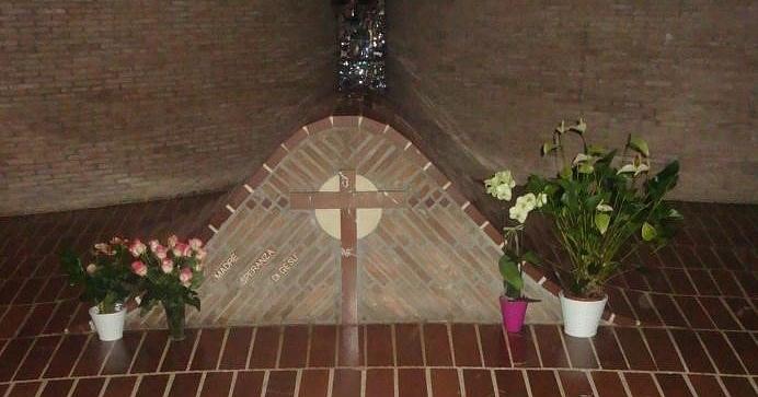 Tomba con croce in mattoni e scritta “Madre Speranza di Gesù”, decorata con fiori in vasi bianchi e colorati