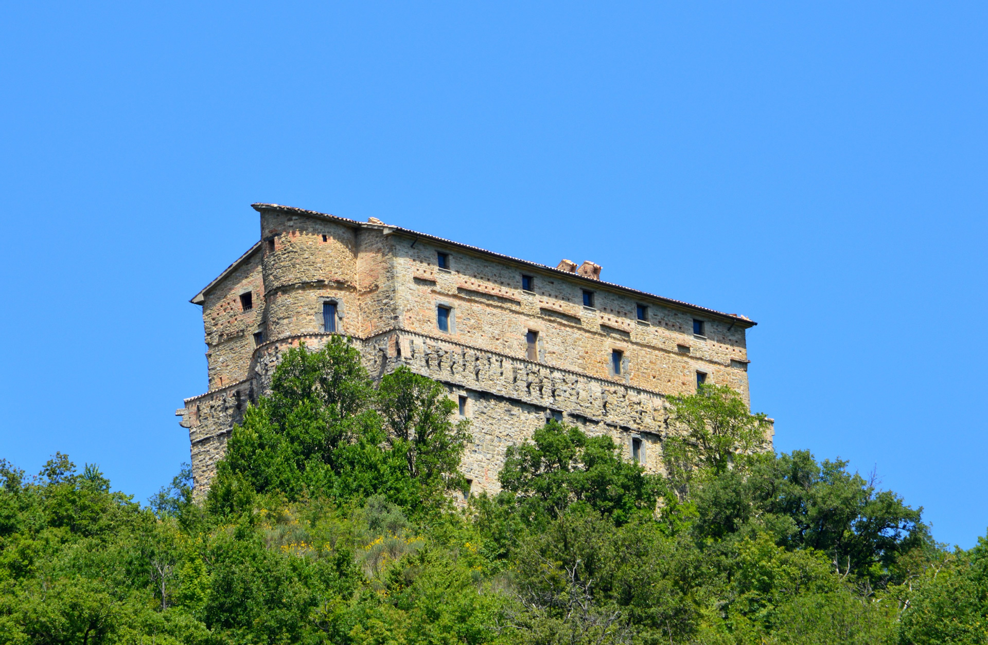 Rocca di Aries à Montone, majestueuse forteresse médiévale émergeant de la végétation sous un ciel limpide.