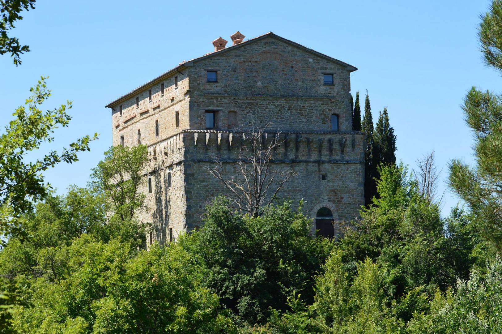 The Rocca di Aries in Montone, imposing stone building emerging from the greenery of the hill under a serene sky.