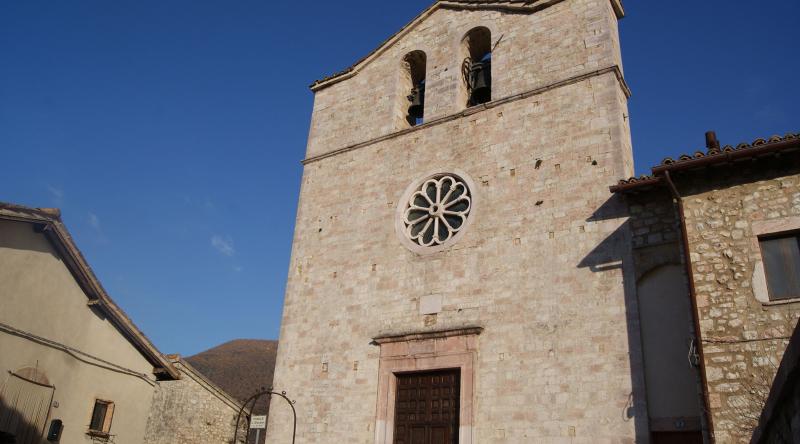 Steinerne Fassade der Kirche San Giovanni Battista in Vallo di Nera mit Glockengiebel, zentraler Rosette und klarem Himmel.