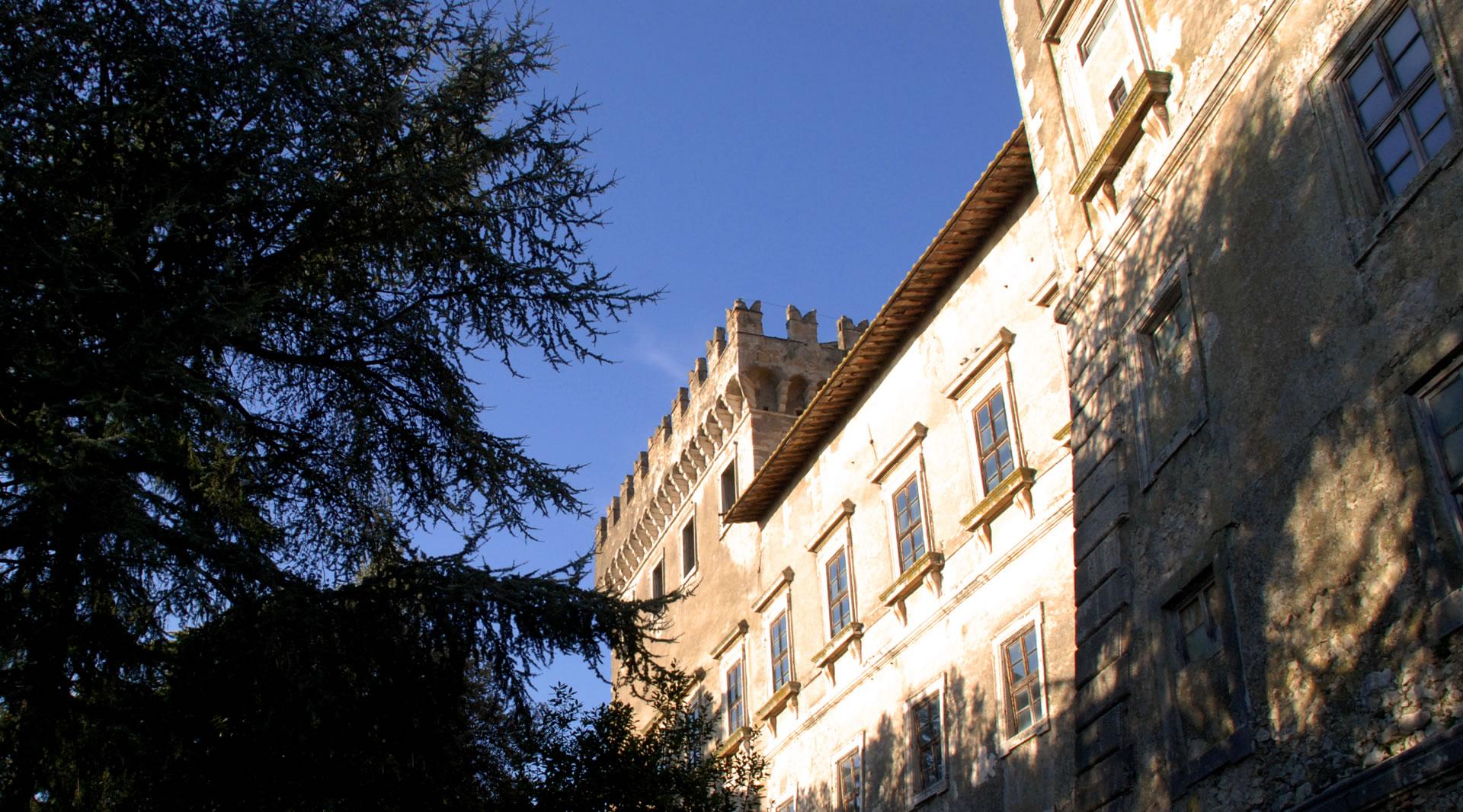 Die sonnenbeschienene Fassade von Schloss Giove zwischen Bäumen mit einem Zinnenturm unter blauem Himmel.
