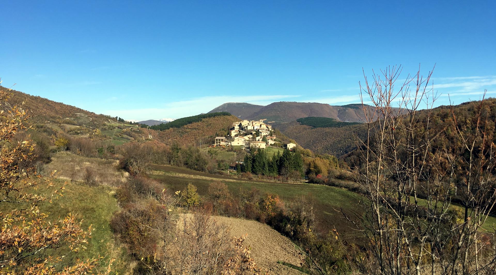 Vista del castello di Usigni poggiato sull’altura circondata da verdi montagne con vegetazione autunnale e un cielo limpido