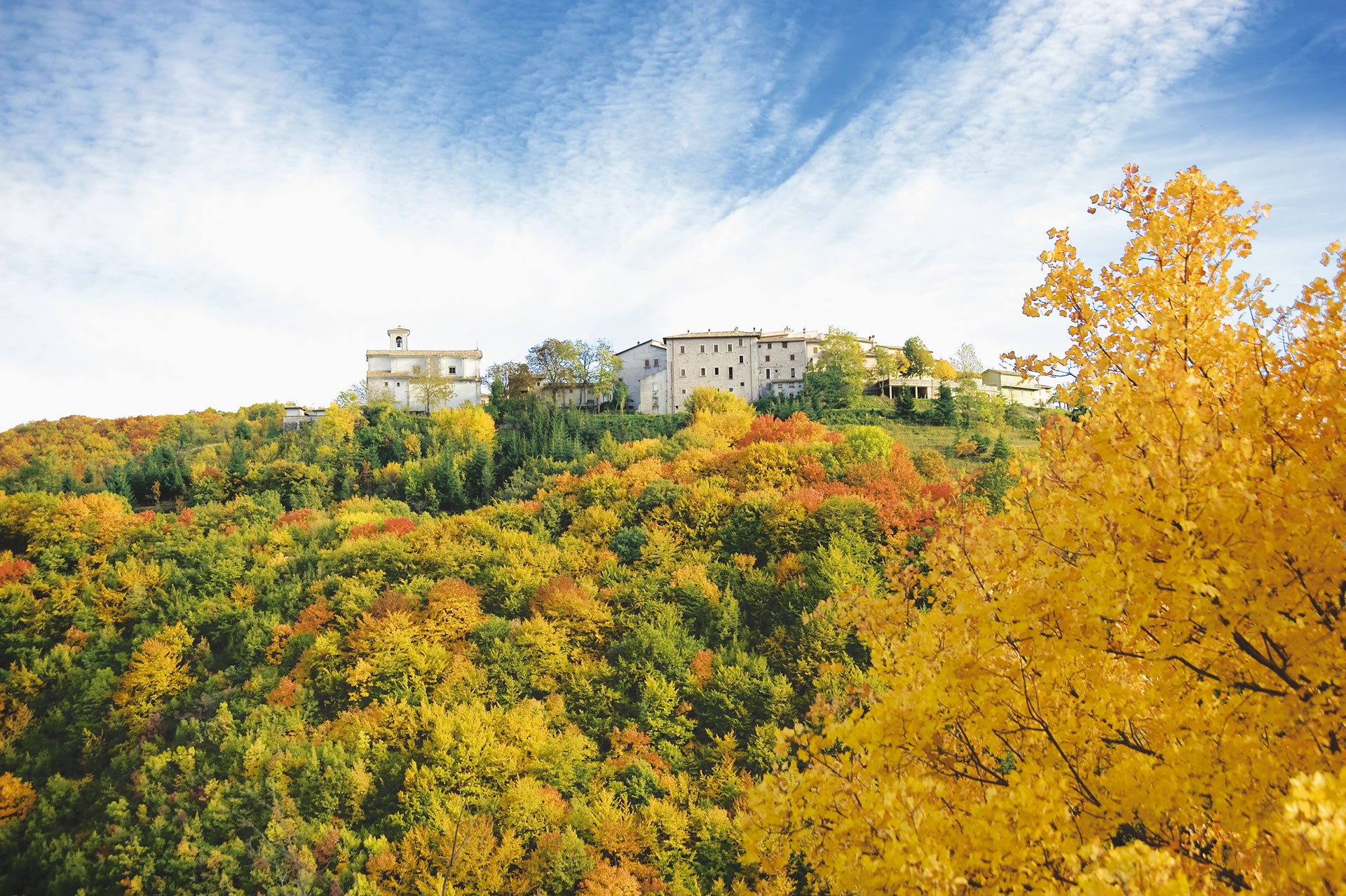 Blick auf Usigni, eingebettet in herbstlich gefärbte Vegetation. Links ist die Kirche San Salvatore zu sehen.