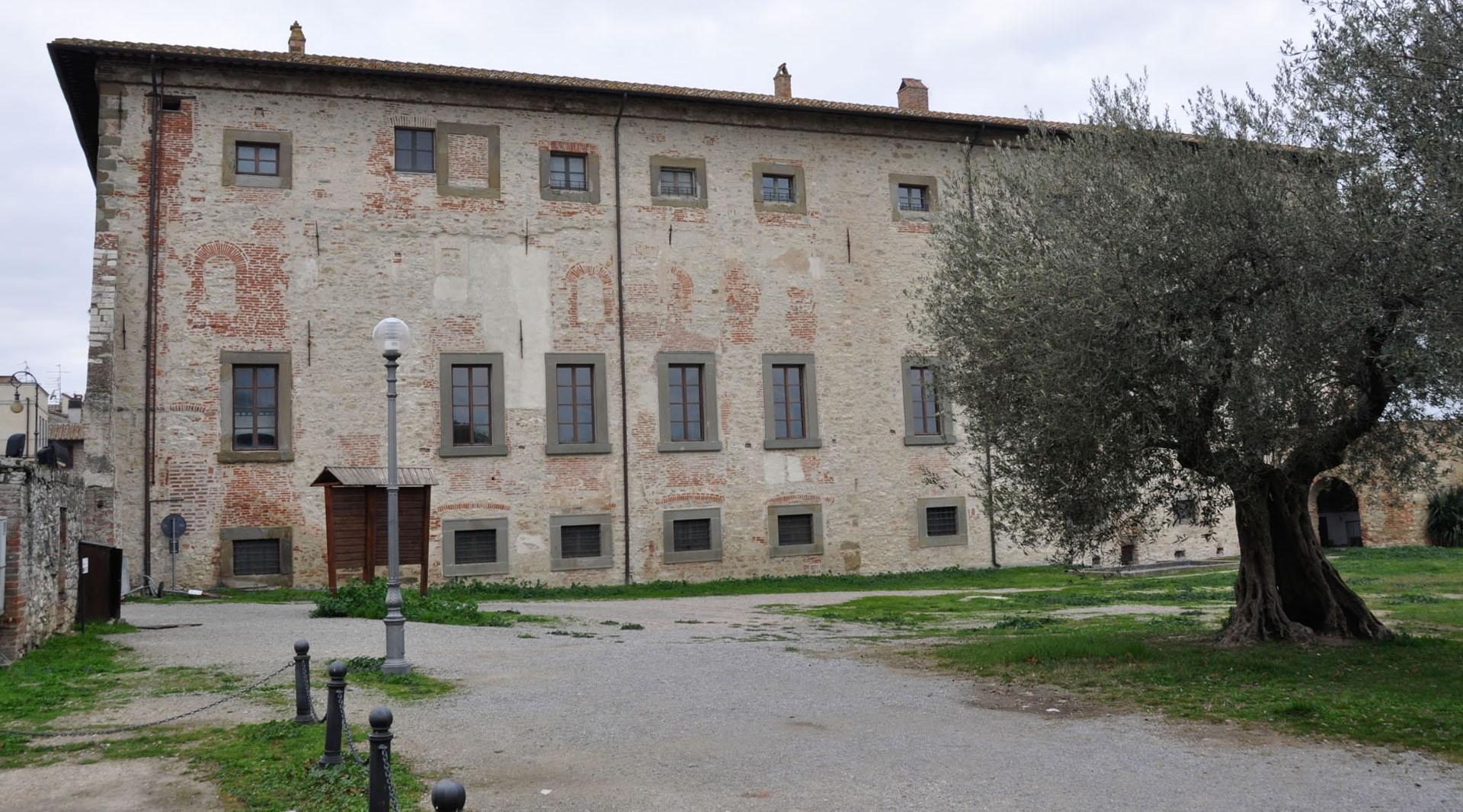 Side view of the Palazzo della Corgna in Castiglione del Lago, with stone and brick façade. A centuries-old olive tree stands beside the building.