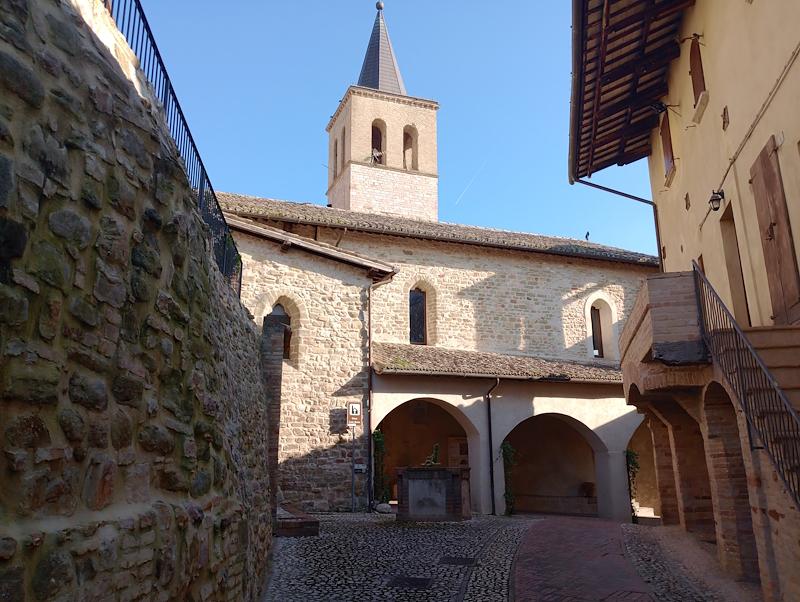 Vicolo acciottolato con pozzo di fronte all’ingresso porticato della chiesa di Santa Marina, con il campanile sullo sfondo