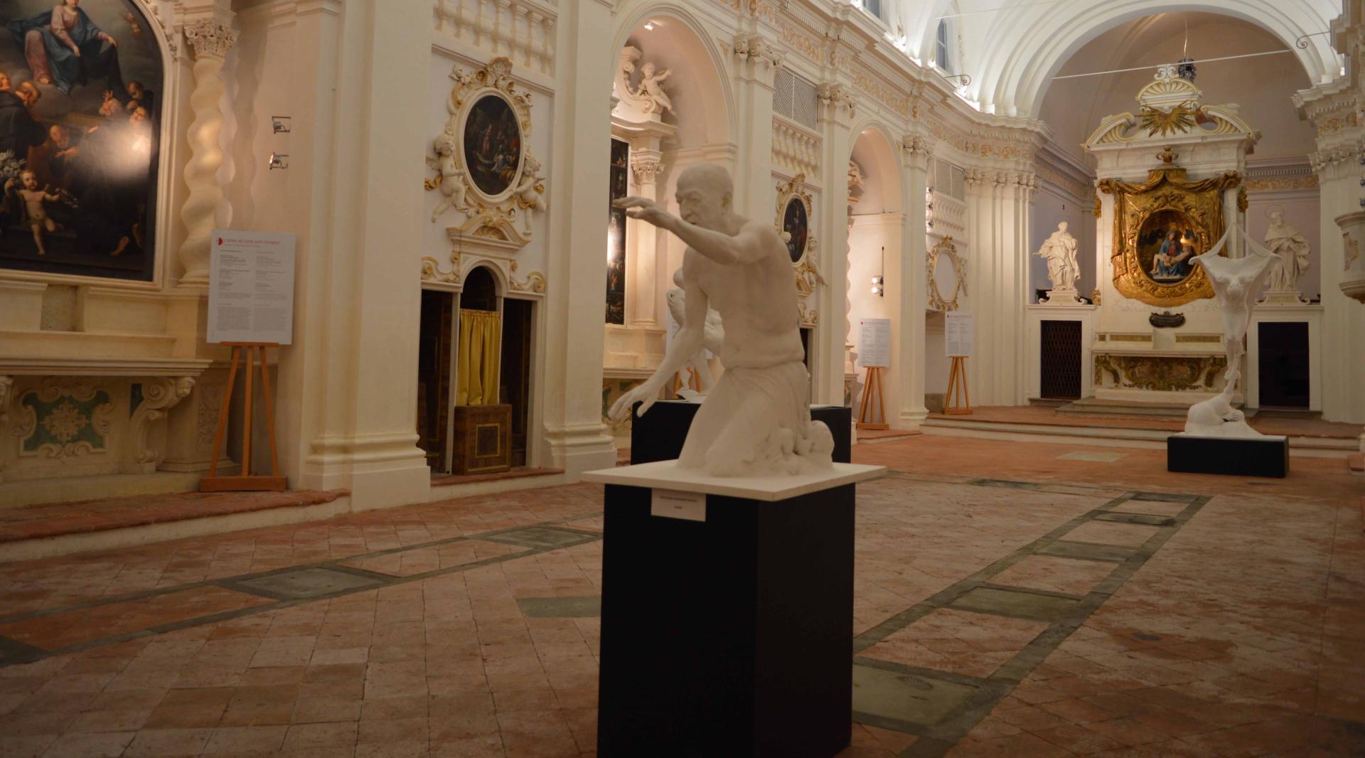 Internal view of the Church of Santa Maria dei Servi, characterized by stucco decorations in Baroque style, a wooden choir, and a large sacristy cabinet. Inside the church, various sculptures are placed in the center of the hall. In the background, the Baroque altar is flanked by two stucco statues in the Bernini style.