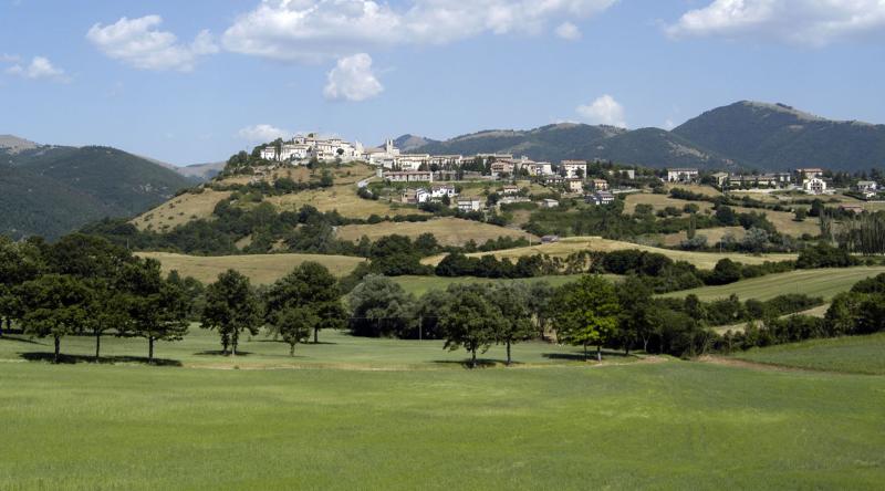 Panorama di Monteleone di Spoleto: il borgo sorge su un colle verde, incorniciato da boschi e montagne appenniniche.