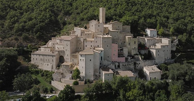 Veduta aerea del Castello di Postignano, frazione di Sellano, con case in pietra arroccate tra i boschi umbri.
