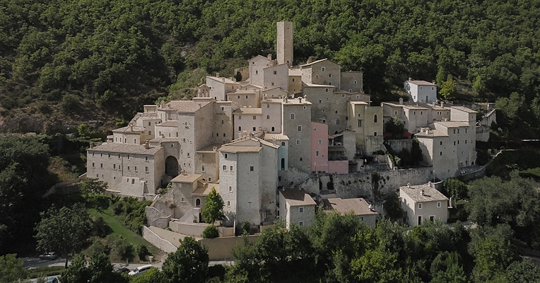 Aerial view of the Castello di Postignano, a hamlet of Sellano, with stone houses perched among the Umbrian woods.