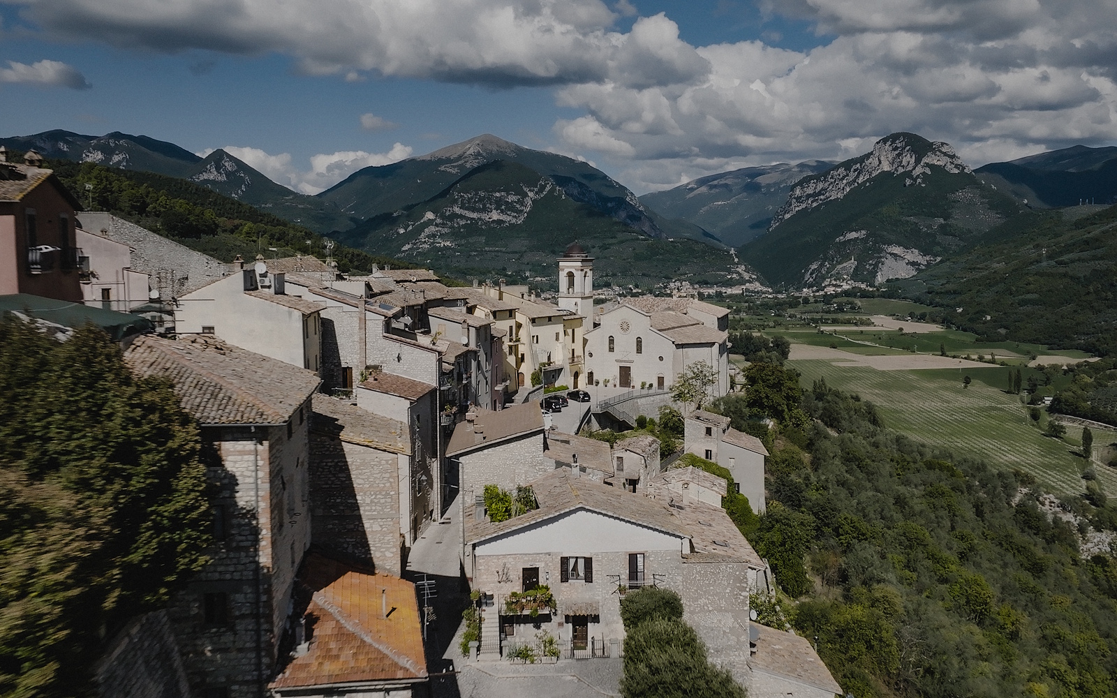 Vue aérienne de Montefranco, village perché d’Ombrie avec église centrale, toits en pierre et montagnes verdoyantes en arrière-plan.