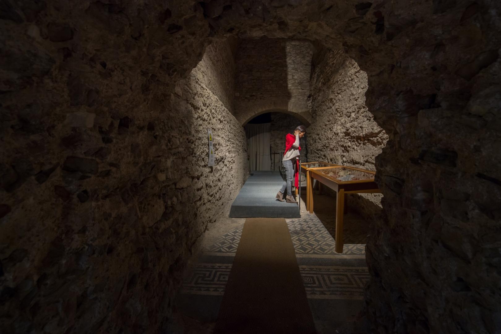 View of the interior of the Roman house in Spoleto, with a person looking at one of the display cases containing objects from the archaeological excavation