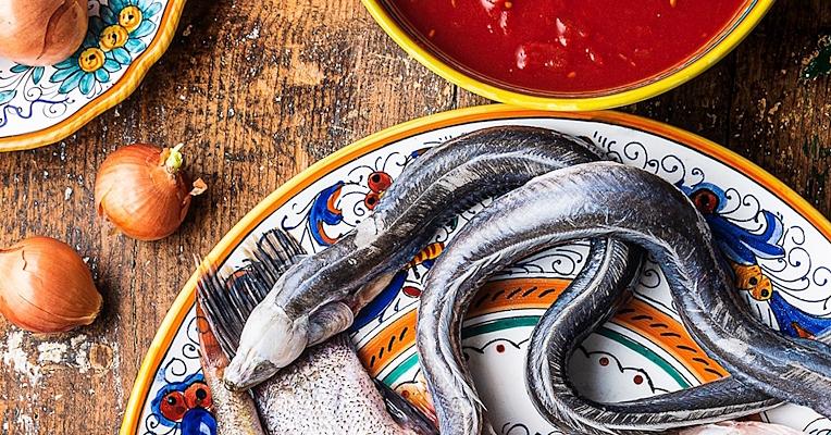 Anguille et poisson de lac sur une assiette décorée, avec des oignons et de la sauce tomate, sur une table en bois rustique.