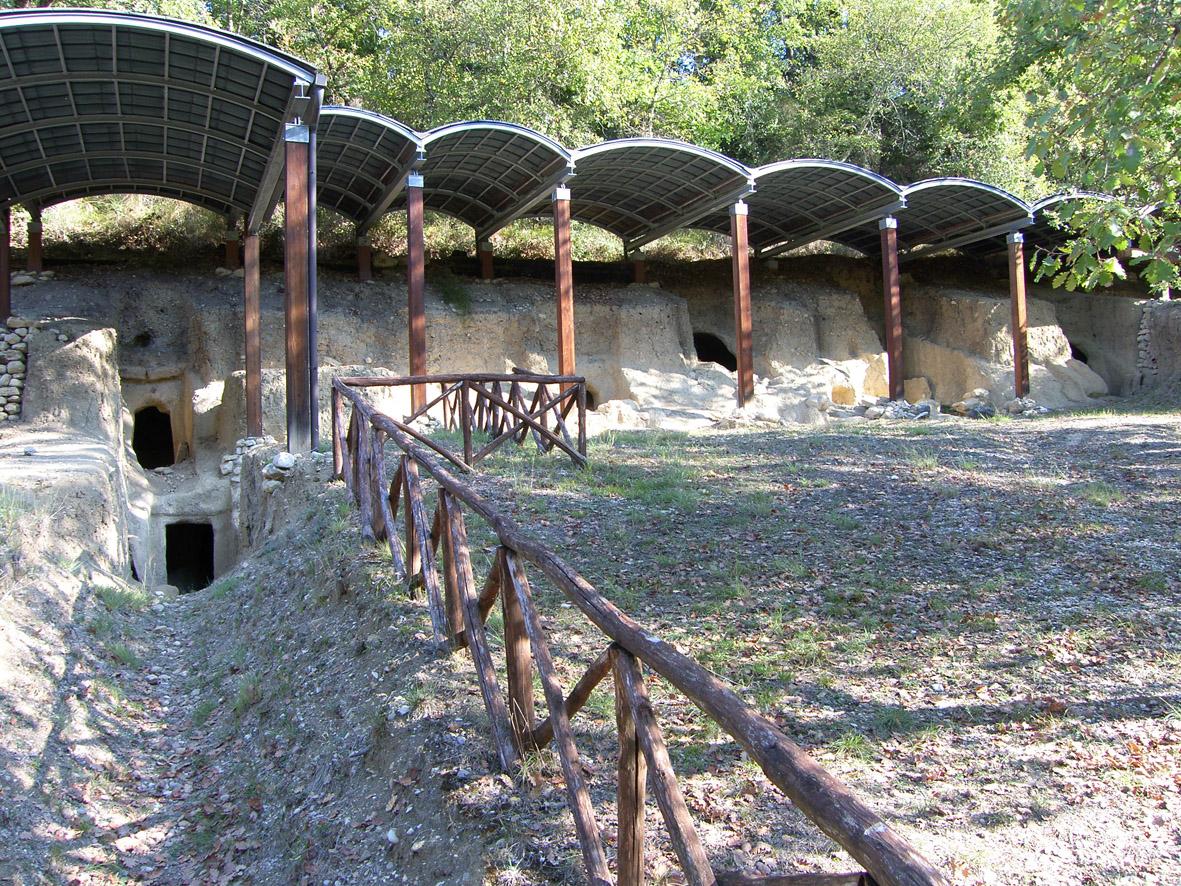 Entrance to Etruscan rock-cut tombs, protected by a shelter and surrounded by trees.