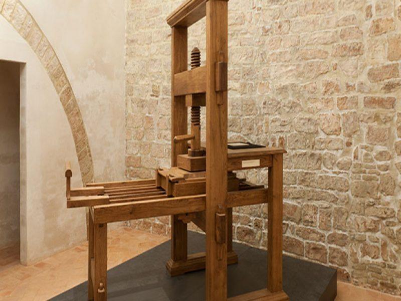 Ancient wooden printing press displayed in a room with stone walls.