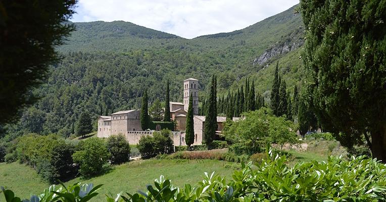 L'Abbaye de San Pietro in Valle entourée de verdure, de cyprès et de collines boisées.