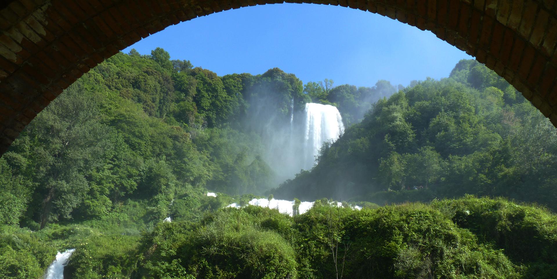 The Marmore Waterfall framed by a brick arch, surrounded by vegetation and set against a clear sky.