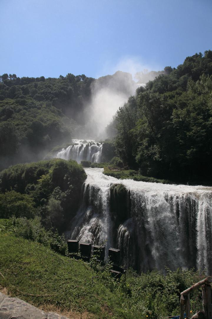The Marmore Waterfall with its cascades of water, framed by dense trees under a bright blue sky.