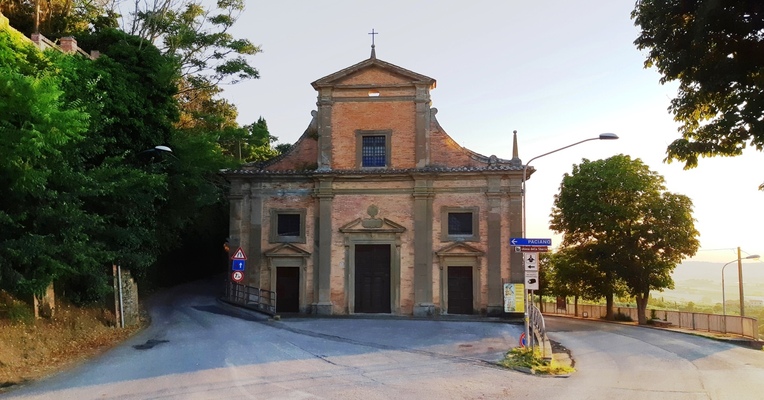 A small brick church, surrounded by trees, is located at a crossroads with street signs.