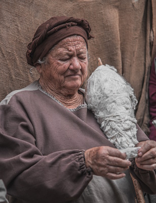 Image of a lady holding a spool with tufts of wool in her arms, as she works on a tuft of wool yet to be spun Credits photo: Francesco Andreoli