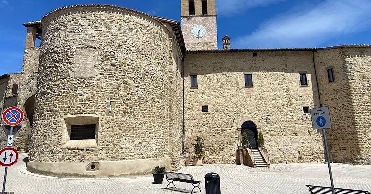 Torre circolare in pietra della chiesa di Santa Marina con campanile, affacciata su una piazza con panchina