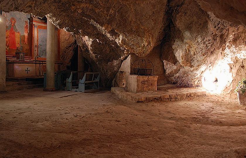 Inneres der Höhle der Einsiedelei Madonna del Riparo mit Freskenaltar, Holzbänken und altem Steinbrunnen.
