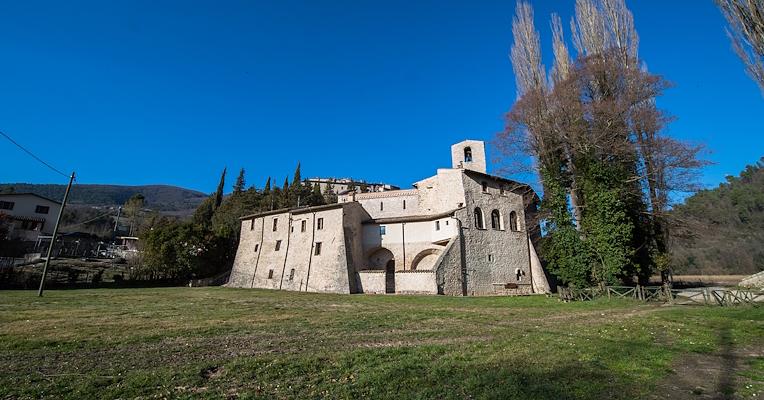 Side view of the Abbey of Saints Felix and Maurus in Castel San Felice, surrounded by greenery at the foot of the Valnerina mountains.