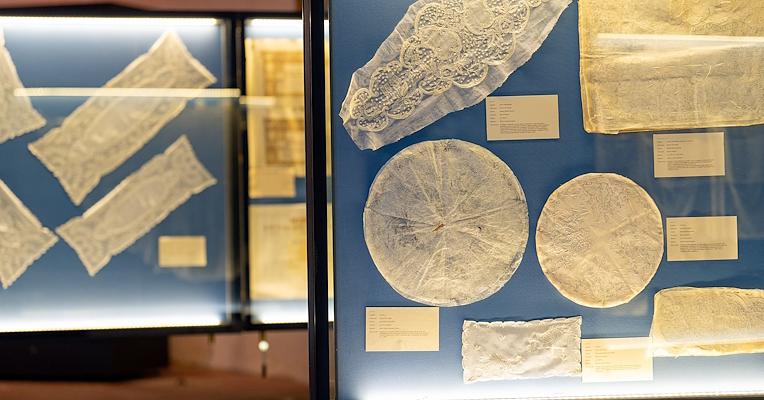 Display case in the museum featuring tulle embroidered items, including doilies and circular and rectangular decorations.