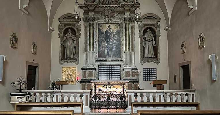 Interior chapel with altar, statues on each side, and a central painting, viewed from wooden pews; serene atmosphere with vaulted arches.