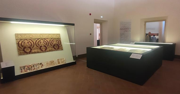 Interior of the sacred vestments room featuring the Antependium in red and gold displayed in a case and an altar frontal in the foreground
