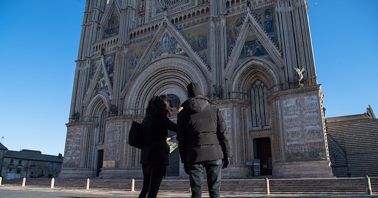 Zwei Personen betrachten die Fassade der Kathedrale von Orvieto, die sich vor einem klaren und heiteren Himmel abzeichnet