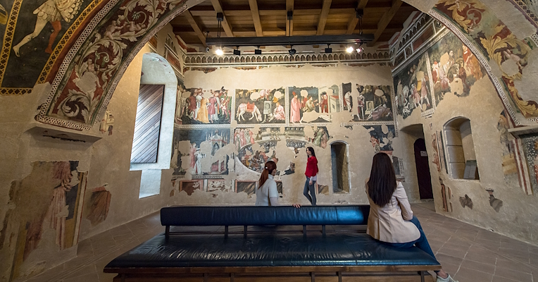 Das Innere der Camera Pinta der Rocca Albornoziana in Spoleto mit Besuchern, die die mit Fresken geschmückten Wände betrachten