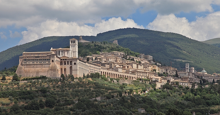 Panoramic view of Assisi featuring the Basilica of Saint Francis and historic buildings in the foreground, with Mount Subasio in the background