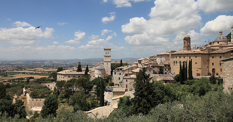Panorama of Assisi with historic stone buildings, bell towers and turrets under a clear sky with some clouds