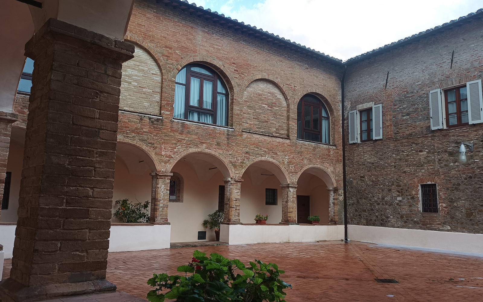 Cloister of the Monteripido Convent, with brick arches, columns and potted plants on a terracotta floor.