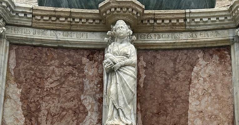 Sculpture of Domina Lacii on the Fontana Maggiore in Perugia, holding some dace fish, with Latin inscriptions on the marble.