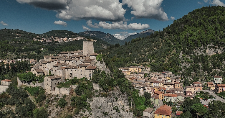 Aerial view of a medieval village on a rocky spur, surrounded by hills and mountains.