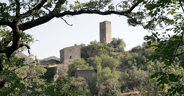 Ancient stone tower on a hill, surrounded by medieval ruins and lush vegetation.
