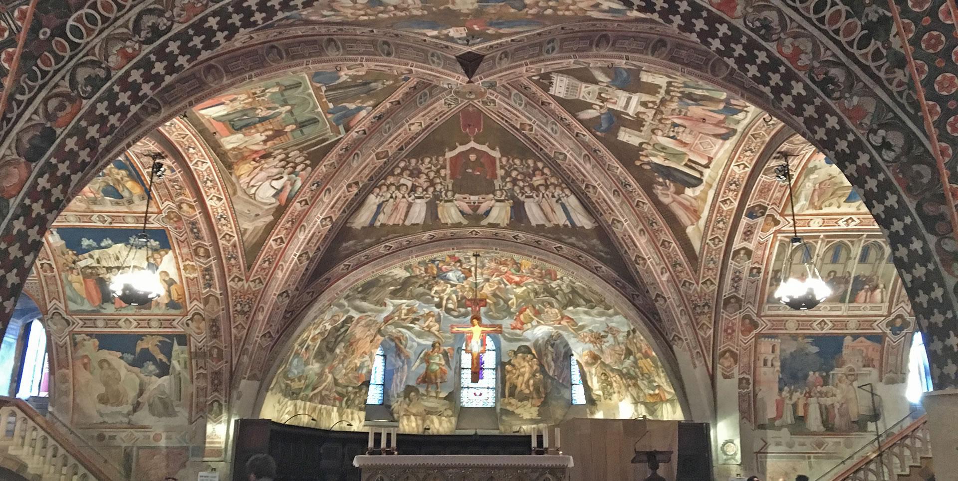 Interior of the Lower Basilica of St Francis in Assisi, with a richly frescoed vault. The frescoes depict religious scenes. The ceiling and walls are finely decorated with Gothic motifs.