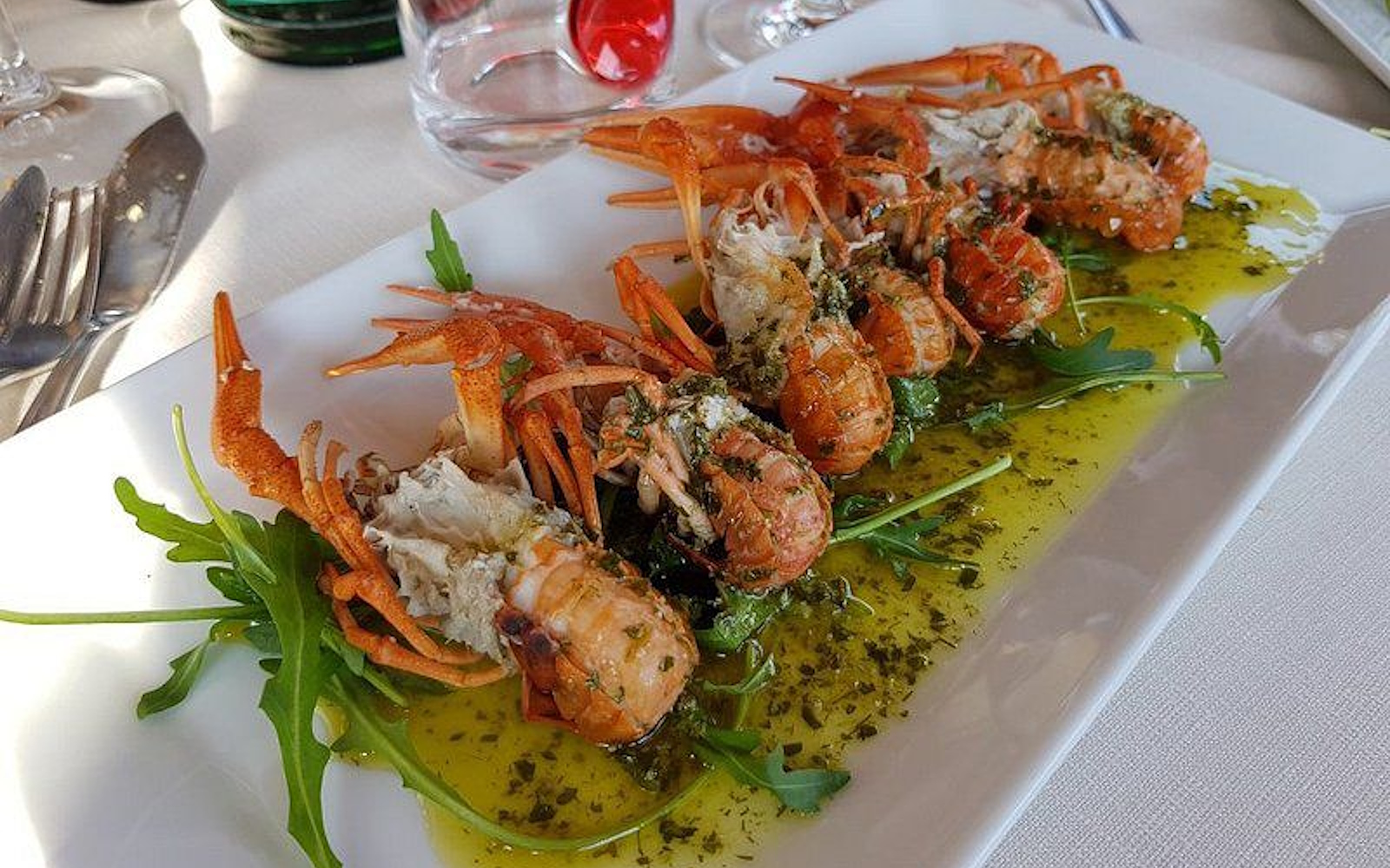 Prawns served on a bed of rocket with green herb sauce, plated on a white dish in an elegant restaurant. (Photo credits: TRATTORIA TERESA)