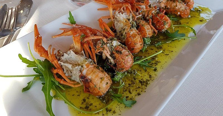 Prawns served on a bed of rocket with green herb sauce, plated on a white dish in an elegant restaurant. (Photo credits: TRATTORIA TERESA)