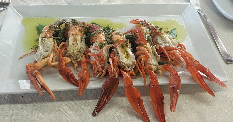 Crevettes servies sur un lit de roquette avec sauce verte, dressées sur un plat blanc dans un restaurant élégant.