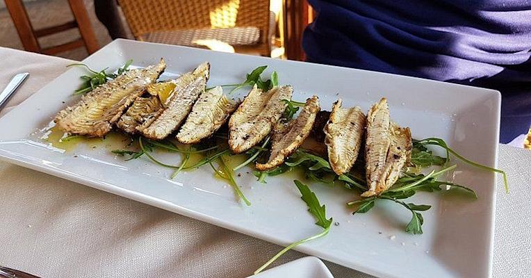 Filets de poisson de lac grillés (carbonaretti), servis sur un lit de roquette avec huile d’olive vierge extra, sur plat blanc. (Photo credits : TRATTORIA TERESA)