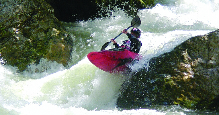 A man paddles a red kayak through a rapid on a river