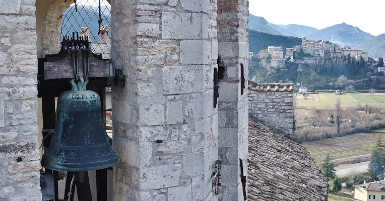 Bronze bell in a bell tower, with a medieval castle in the background