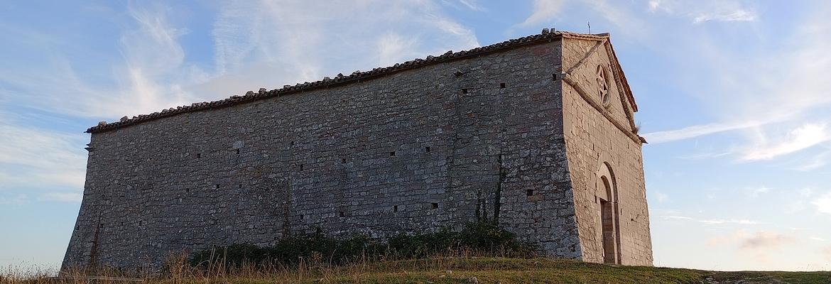 Side view of a stone building located on a grassy hill, with a blue sky and light clouds in the background.