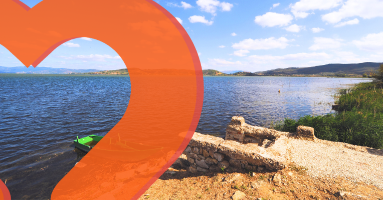Small beach and stone pier with a green boat on Lake Trasimeno in Magione, with hills in the background.